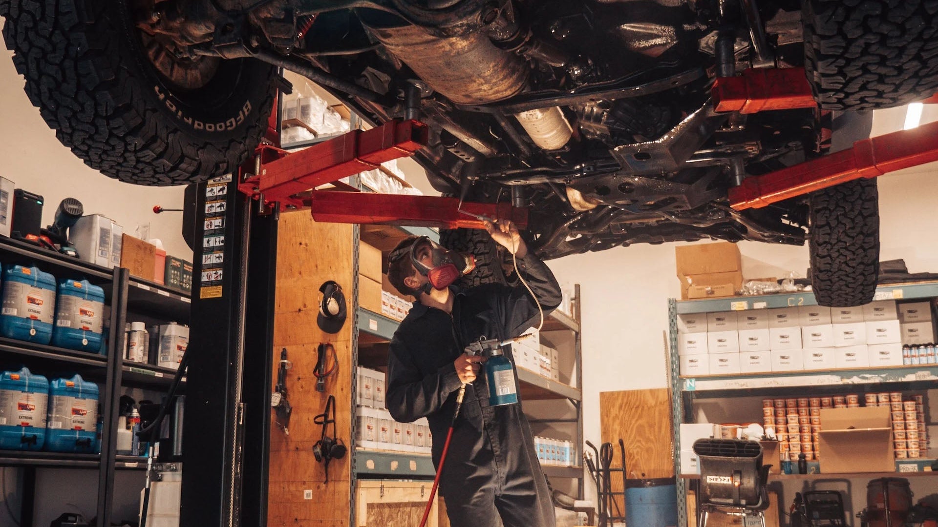 Mechanic working on a vehicle under a lift in a garage.